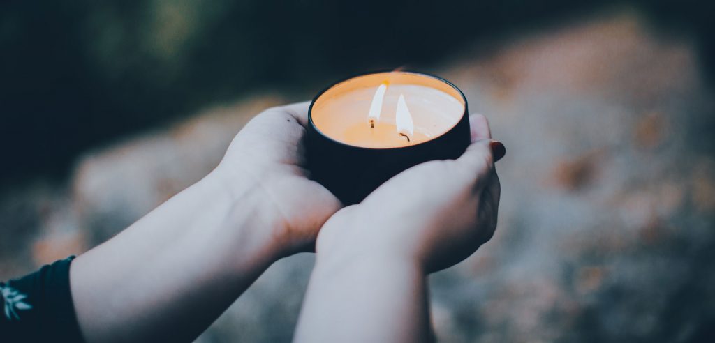 two hands holding a tea light candle